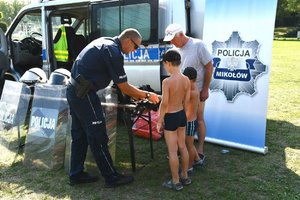 policjant pokazujący dzieciom i mężczyźnie elementy policyjnego wyposażenia