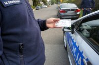 Policjant mikołowskiej drogówki wręcza jednemu z kierujących zapachową zawieszkę.