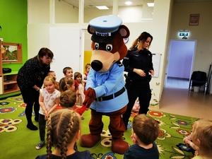 sala w przedszkolu, na środku stoi policyjna maskotka, wokół niej dzieci, obok policjantka