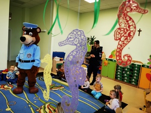 sala przedszkolna, na dywaniku dzieci, policyjna maskotka i policjantka