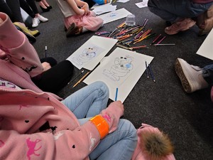 leżące na dywanie kolorowanki, obok dzieci, porozrzucane kredki